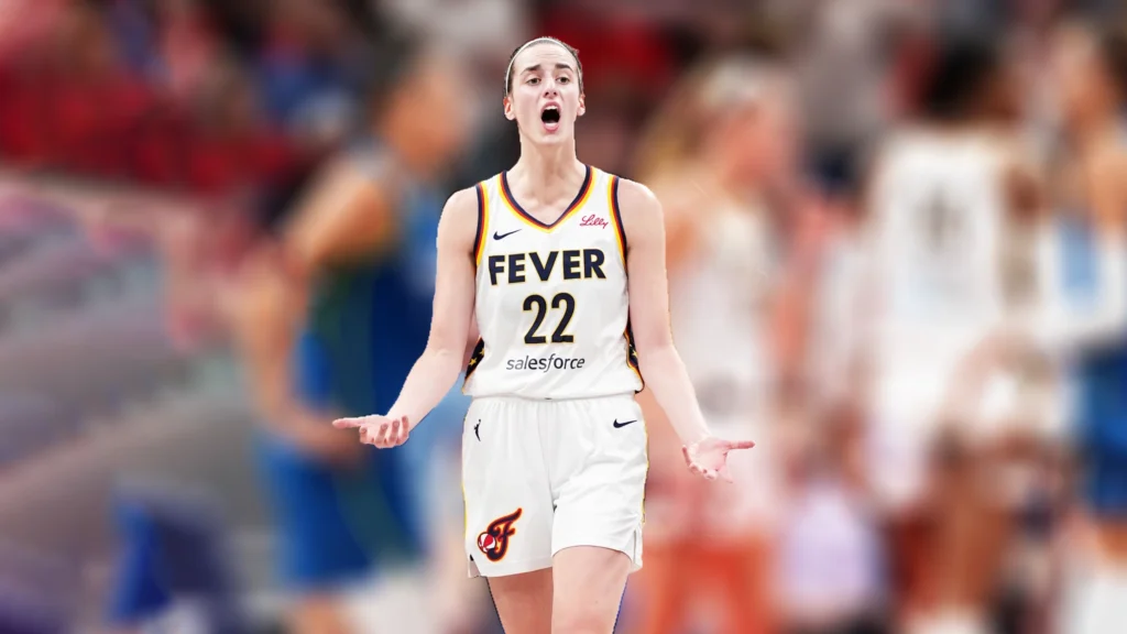 A female basketball player, Caitlin Clark, in a white Indiana Fever jersey with the number 22, stands with her mouth open and hands outstretched in a questioning or protesting gesture during a game.