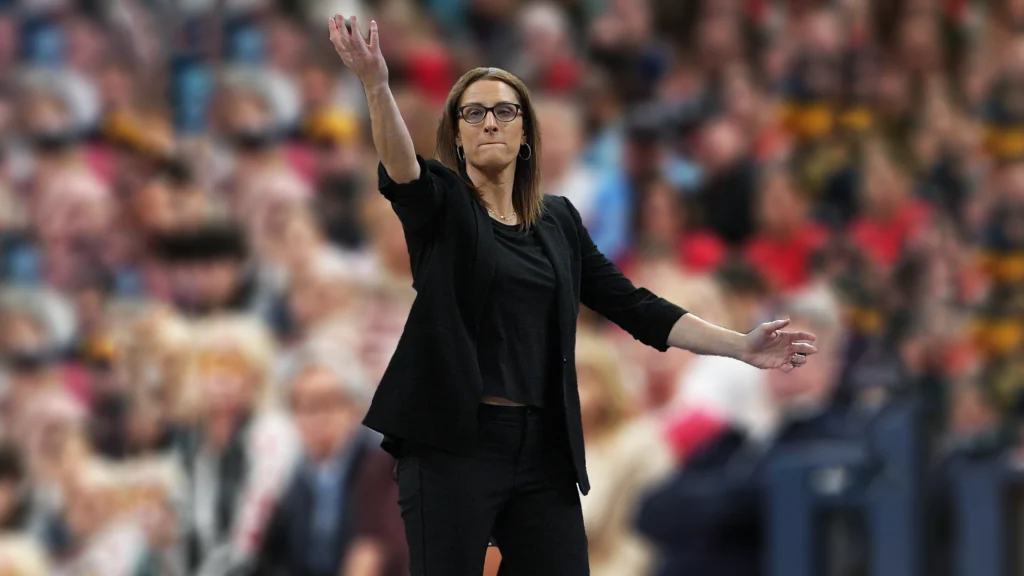 Stephanie White, dressed in a black top and jacket, stands with her arms raised, seemingly coaching intensely during F with a blurred audience behind heever vs Liberty match.