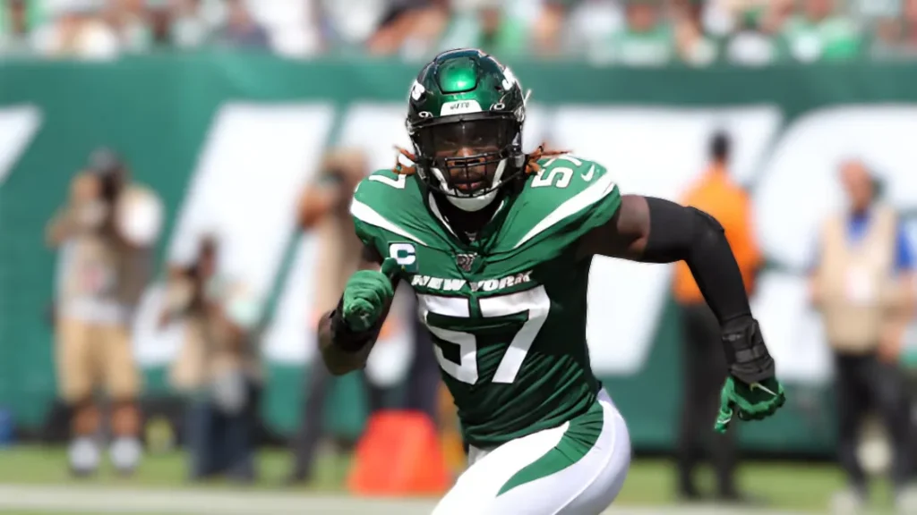 C.J. Mosley, a male football player, in a green New York Jets uniform with the number 57 and a captain's patch. He is running on a bright green football field with a blurred stadium background, looking directly forward.