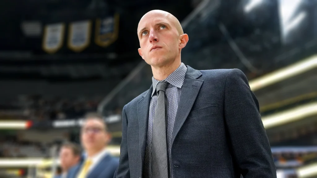 Dan Muse, the newly appointed head coach of the Pittsburgh Penguins, on the bench during a game, deeply focused on the action.