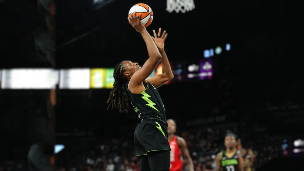 Nneka Ogwumike, wearing a green and black Seattle Storm jersey, shoots a basketball on court with a dark arena background.