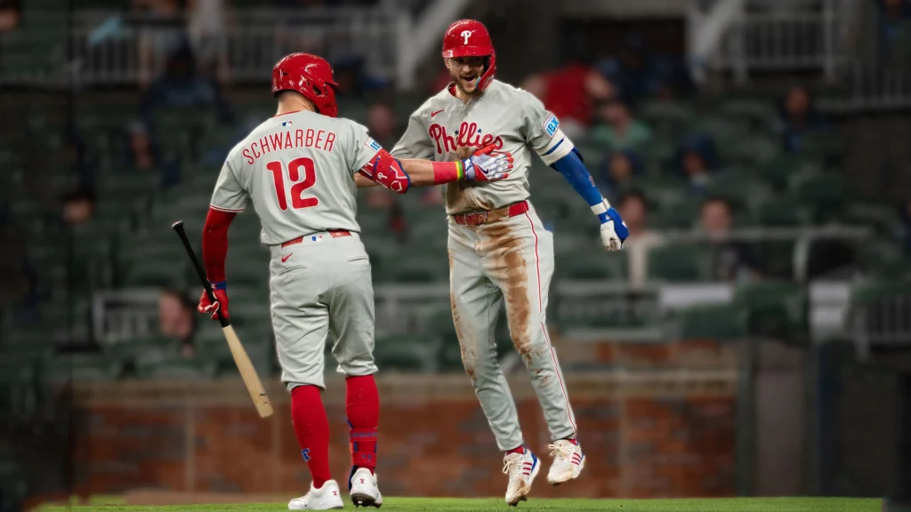 Two Phillies baseball players, Trea Turner and Kyle Schwarber, are high-fiving or fist-bumping on the field.