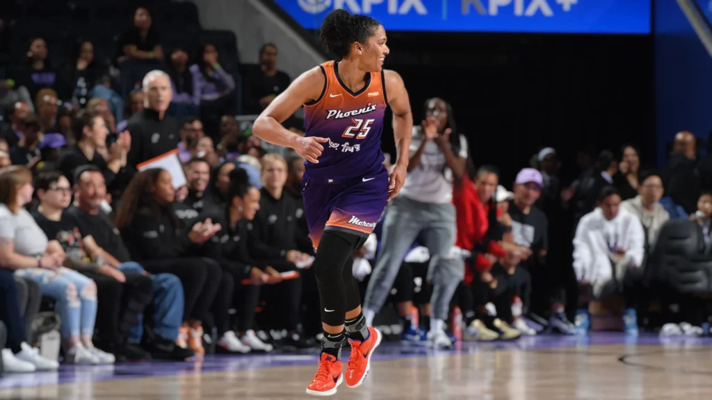 Alyssa Thomas during Valkyries vs Mercury WNBA game, wearing a purple Phoenix Mercury jersey with the number 25, runs on a basketball court with a determined expression, looking towards her left. She has her hair pulled back and is wearing black compression sleeves and bright red sneakers. Spectators are visible in the blurred background.