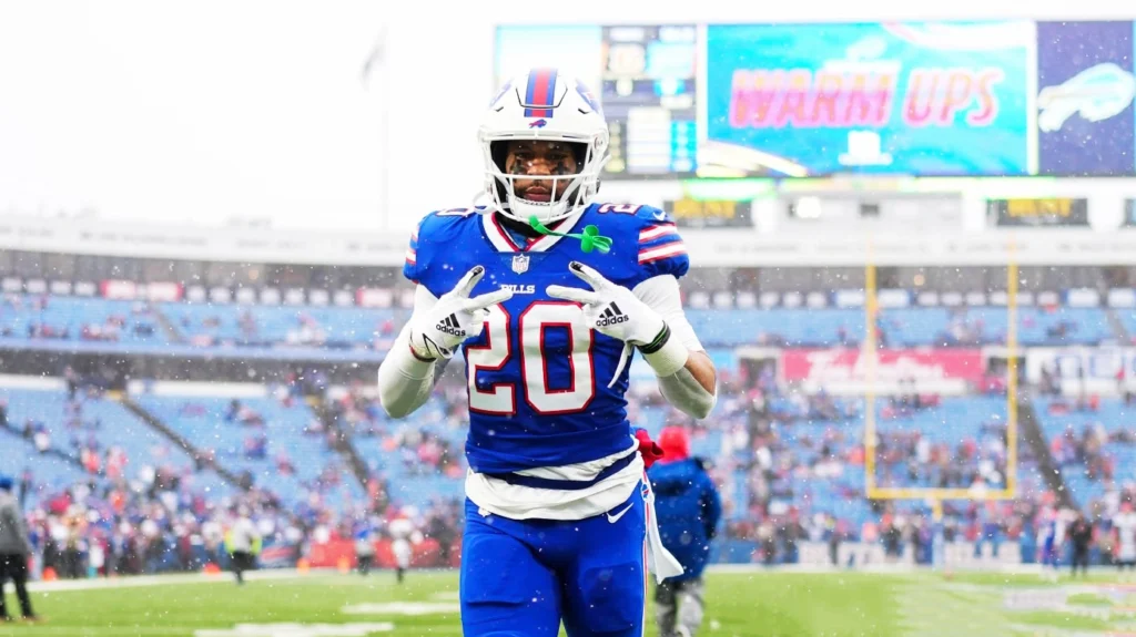 Nyheim Hines, a football player for the Buffalo Bills, standing on a snowy field in a blue uniform with the number 20, making a hand gesture.