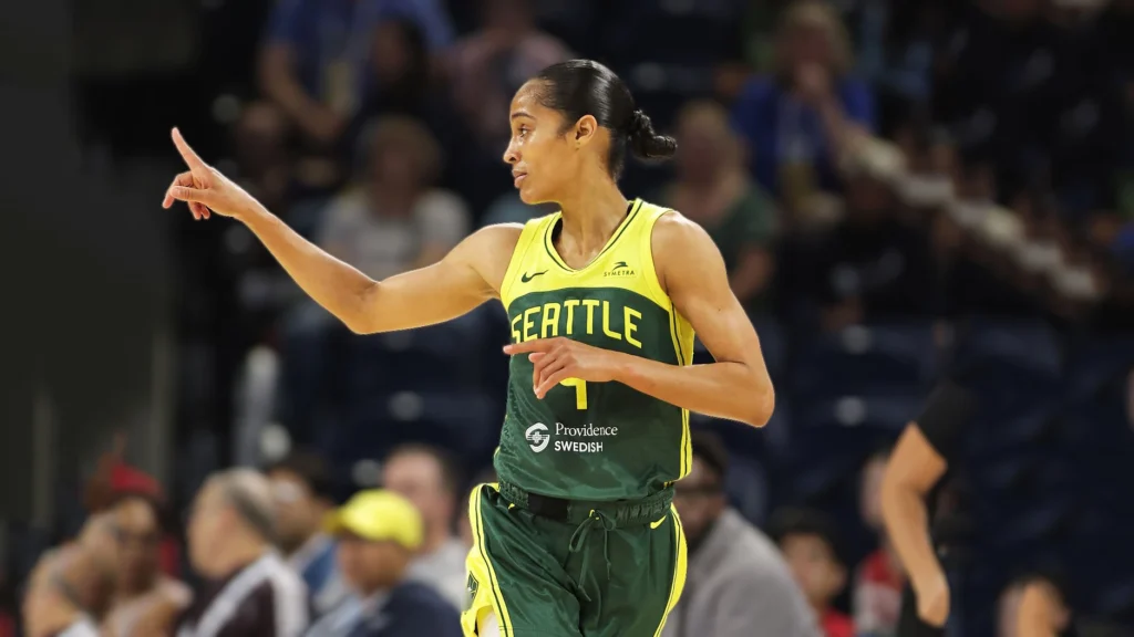 Skylar Diggins-Smith, a player for the Seattle Storm, wearing a green and yellow jersey, points across the basketball court during a game. She is looking to her right with a focused expression, appearing to direct her teammates.