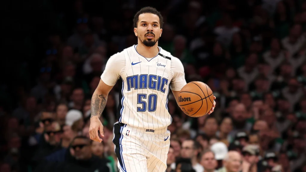 Cole Anthony, wearing an Orlando Magic number 50 jersey, dribbles a basketball on an NBA court with blurred fans in the background.