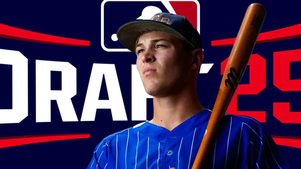 A young baseball player, Eli Willits, wearing a blue and white pinstriped jersey and a baseball cap with "FB" (presumably for Fort Cobb-Broxton) on it, poses confidently while holding a wooden baseball bat over his shoulder. The background features a blurred red and blue graphic with "DRAFT '25" and the MLB logo.