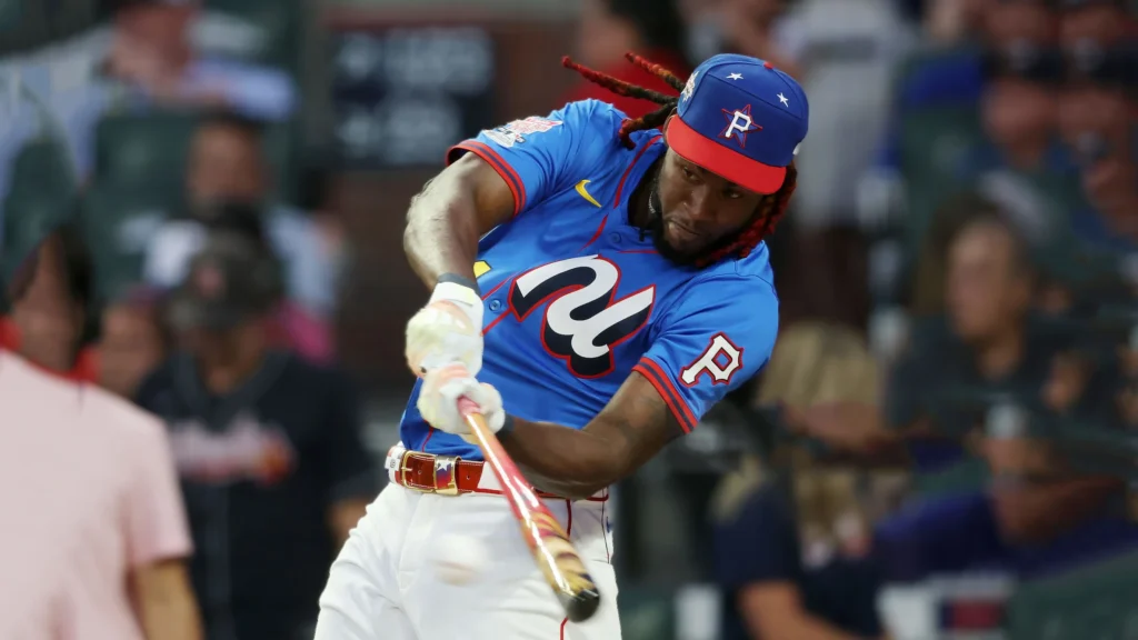 Oneil Cruz, a tall baseball player with long red dreadlocks and a blue and red cap, swings a baseball bat with force while wearing a blue jersey with a red "P" logo and white pants during a game.